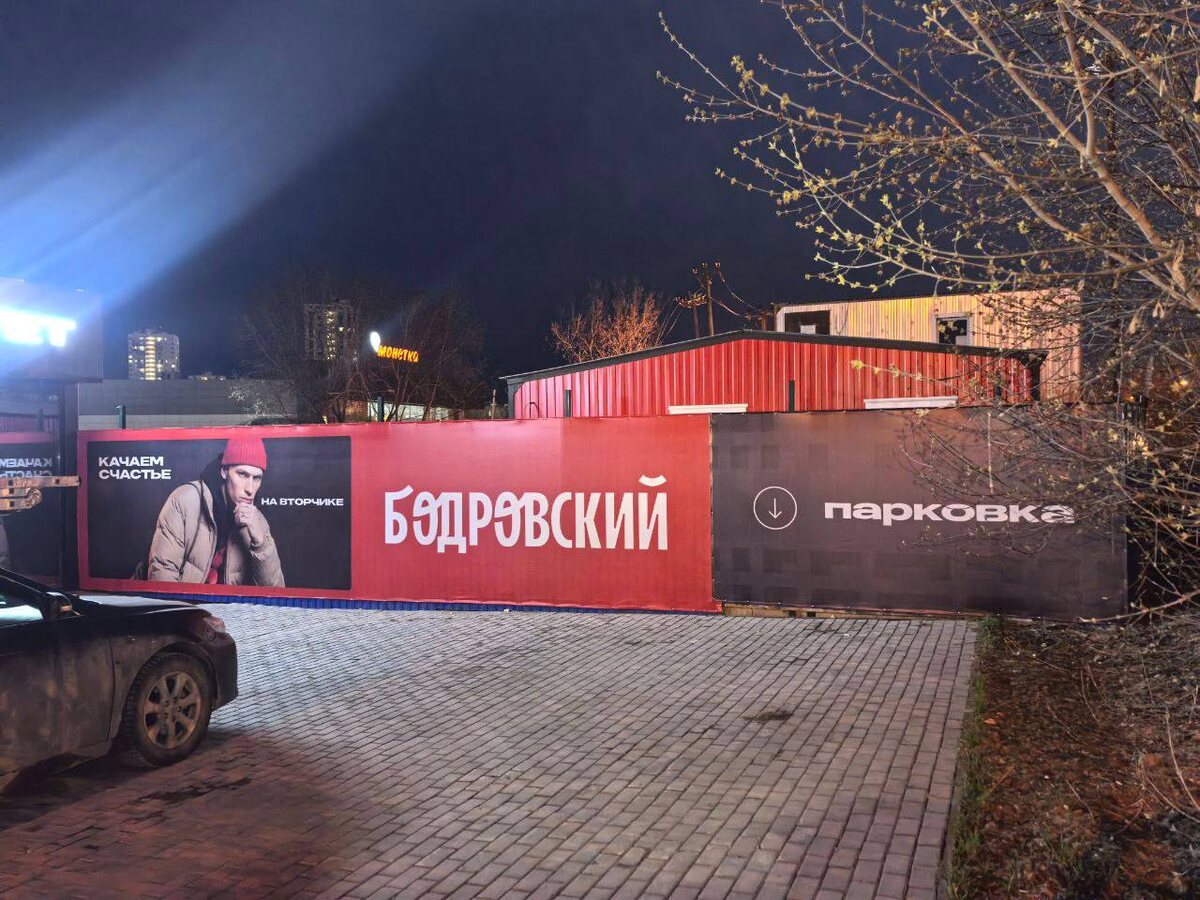 Ограждение ЖК «Бодровский» вечером: модули с названием комплекса и указателем парковки