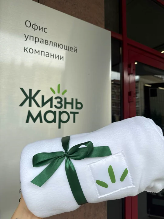Белый плед в рулоне с лентой и нашивкой с логотипом